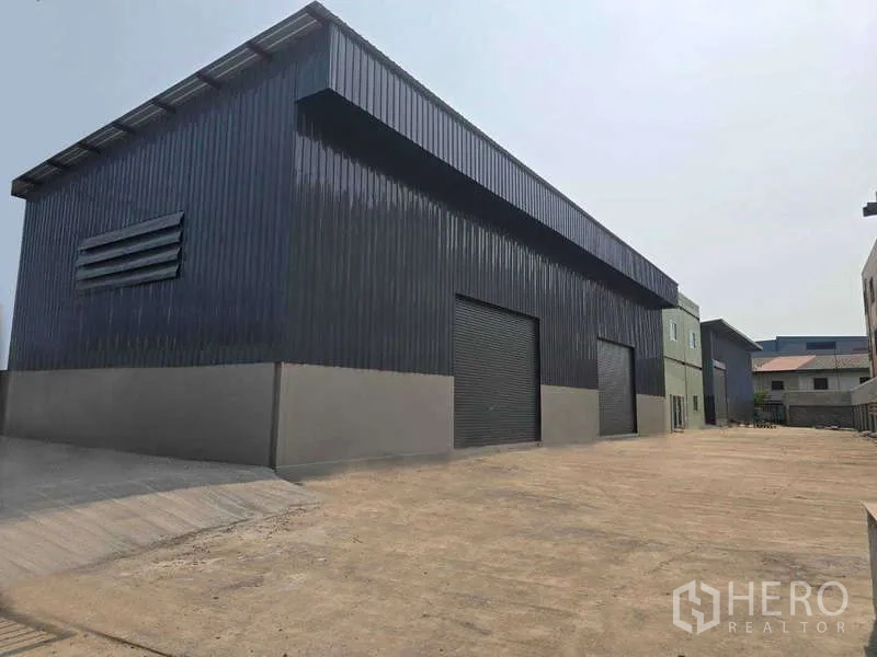Warehouse for rent in Mueang Samut Sakhon, Samut Sakhon - Exterior view of a long black‑clad warehouse with multiple roller shutters and driveway.