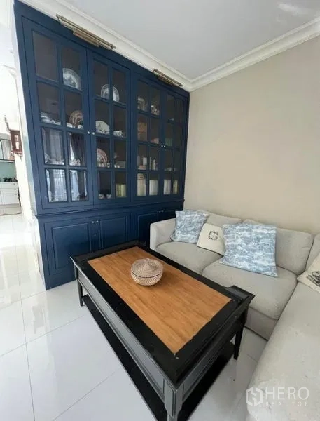 Townhouse for rent or sale in Bueng Kum, Bangkok - Bright living room with L-shaped sofa, navy built-in display cabinet, and glossy floor tiles.