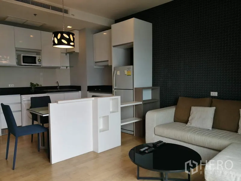Condominium for rent in Watthana, Bangkok - Open-plan living area with sofa, compact dining set and white fitted kitchen.