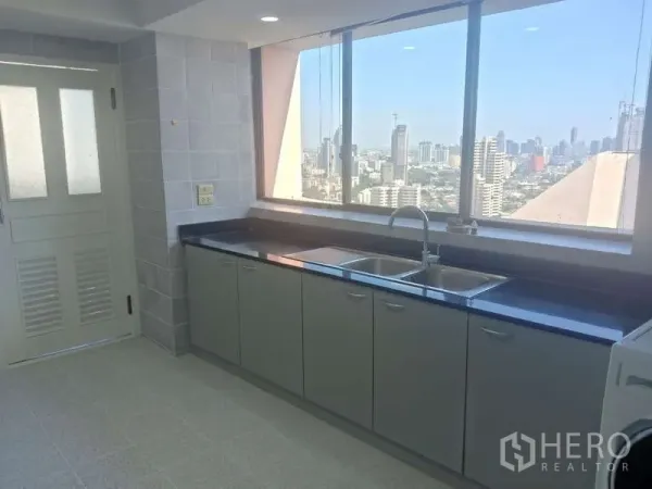 Condominium for rent in Khlong Toei, Bangkok - Bright closed kitchen with long black countertop, double sink, and Bangkok skyline view at President Park.