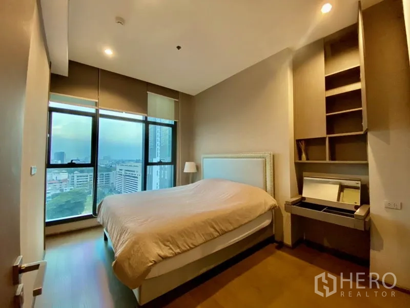 Condominium for rent or sale in Bang Rak, Bangkok - Primary bedroom with large windows, city view, built-in shelves and dressing vanity.