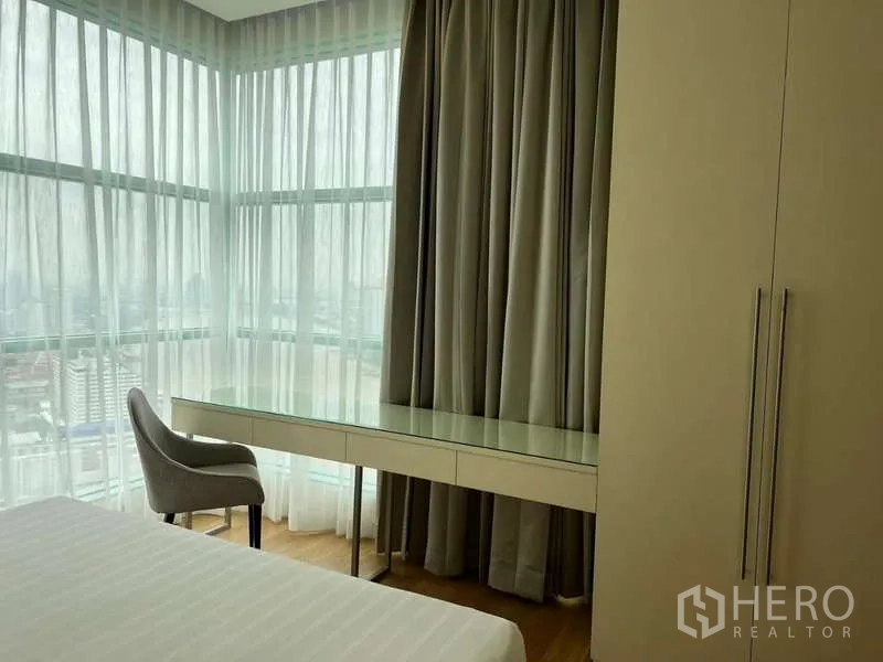 Condominium for rent in Bang Kho Laem, Bangkok - Corner bedroom workspace with long built-in desk and sheer curtains.