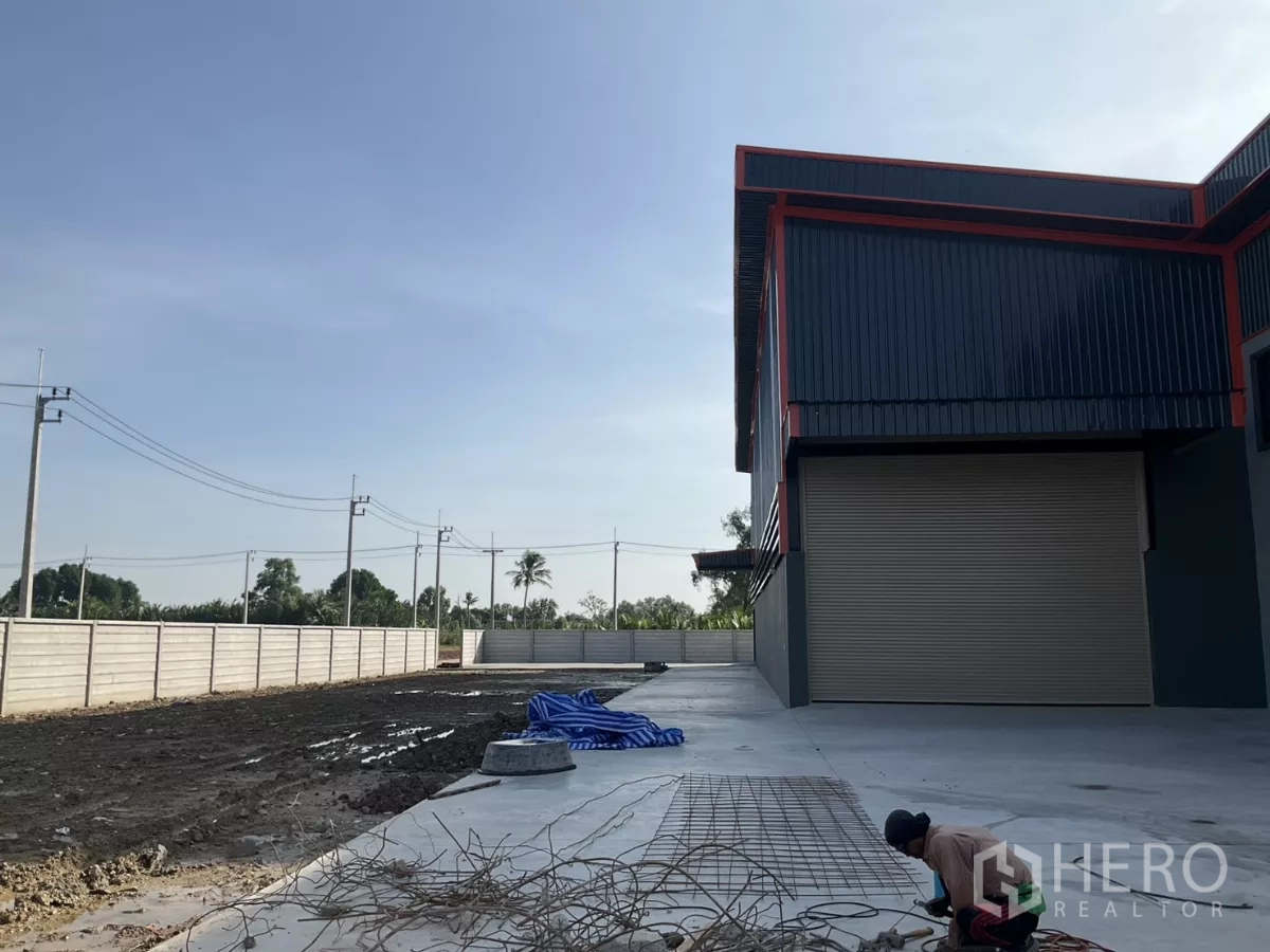 Factory for sale in Samut Sakhon - Side driveway and loading area beside roller shutter door and boundary wall.