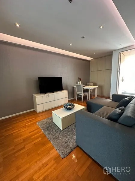 Apartment for rent in Khlong Toei, Bangkok - Cozy living room with sofa, rug, TV unit, and dining nook.