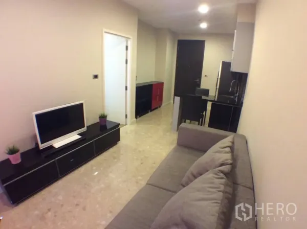 Condominium for rent in Khlong Toei, Bangkok - Cozy living space with sofa, TV console, polished floors, and hallway to the entrance.