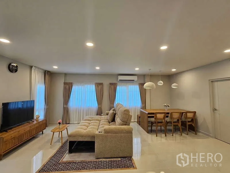 Detached House for rent in Bang Phli, Samut Prakan - Open-plan living and dining room with L-shaped sofa, TV console and large windows.