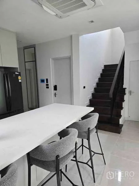 Detached House for rent in Bang Phli, Samut Prakan - Kitchen view toward a dark wood staircase beside the island counter.
