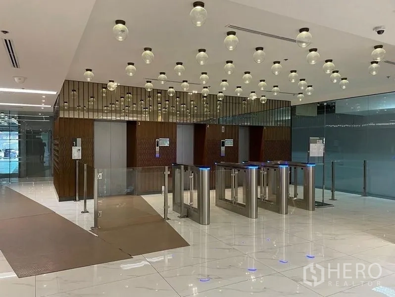 Office Space for rent in Bang Rak, Bangkok - Modern office lobby featuring security turnstiles, elevators and decorative pendant lights on a polished floor.