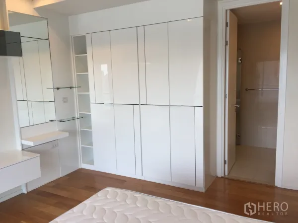 Condominium for rent in Ratchathewi, Bangkok - Bedroom corner showing glossy white closets, vanity shelves, and door to bathroom.