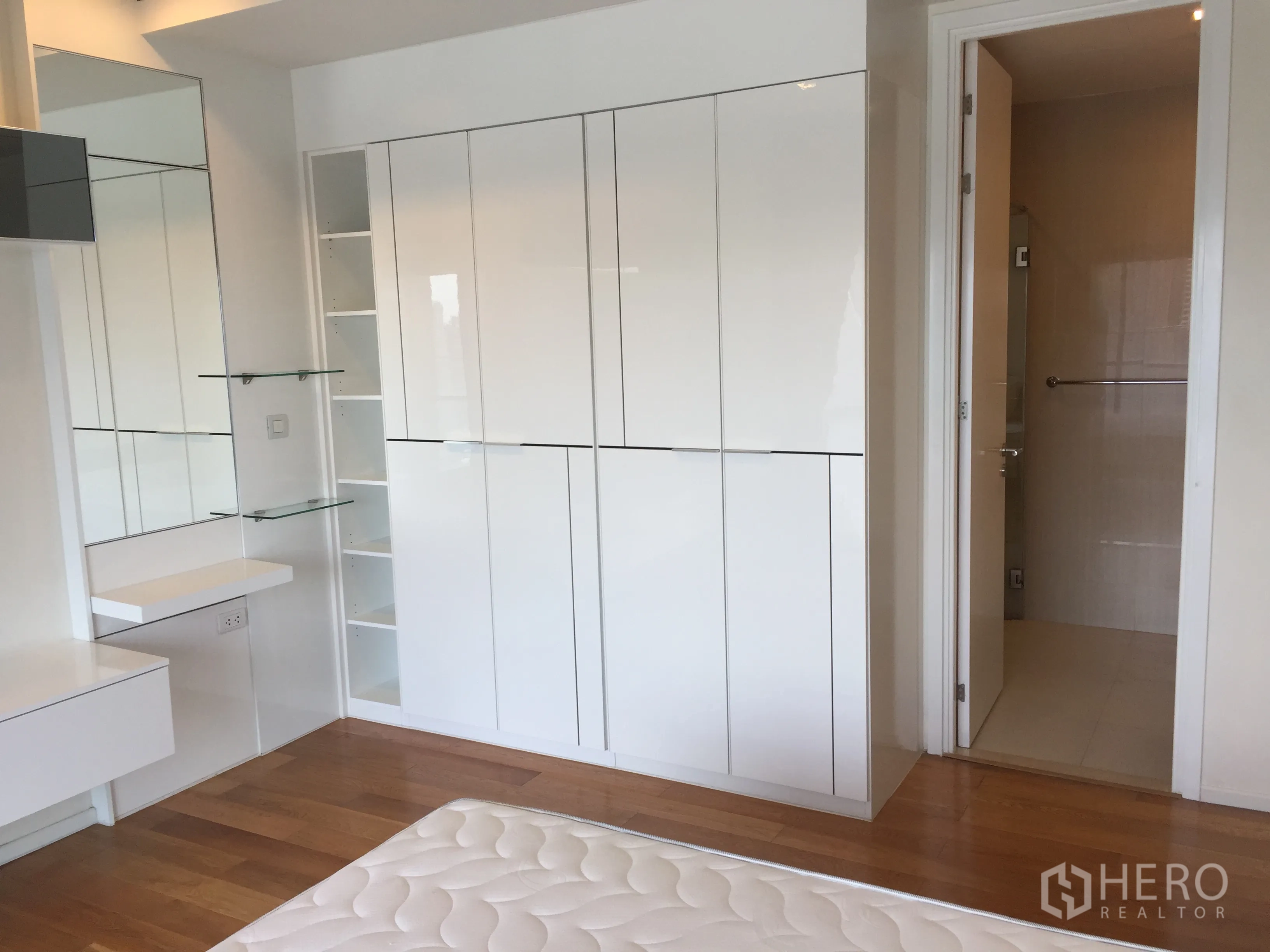 Condominium for rent in Ratchathewi, Bangkok - Bedroom corner showing glossy white closets, vanity shelves, and door to bathroom.