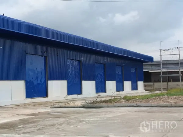 Warehouse for rent in Bang Len, Nakhon Pathom - Side elevation of steel warehouse with multiple blue roller shutter loading doors.