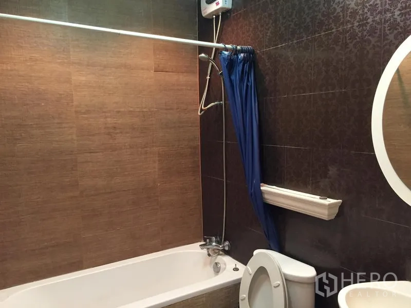 Townhouse for rent in Chatuchak, Bangkok - Bathroom with bathtub, shower over tub, blue curtain and patterned brown wall tiles.
