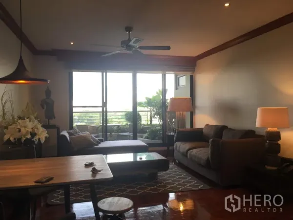 Condominium for rent in Sathon, Bangkok - Bright living area with sofas and pendant light opening onto a plant-filled balcony through sliding glass doors.