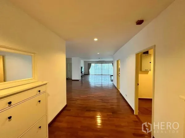 Condominium for rent in Bangkok - Long corridor leading to a bright open-plan living area with wide windows and glossy wood floors.