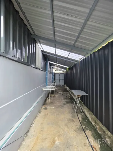 Warehouse for rent in Khlong Toei, Bangkok - Covered service walkway along the warehouse side with metal roof and drainage piping.