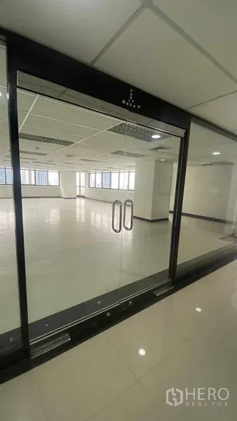 办公空间 出租或出售在Phaya Thai, Bangkok - 黑色框架玻璃门通向空置整层，亮面地坪与网格吊顶灯光。