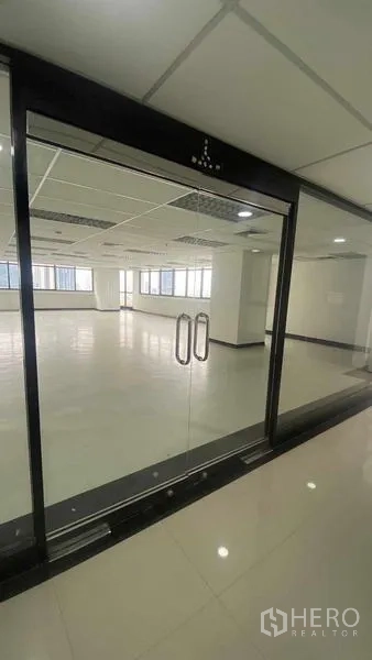 办公空间 出租或出售在Phaya Thai, Bangkok - 黑色框架玻璃门通向空置整层，亮面地坪与网格吊顶灯光。