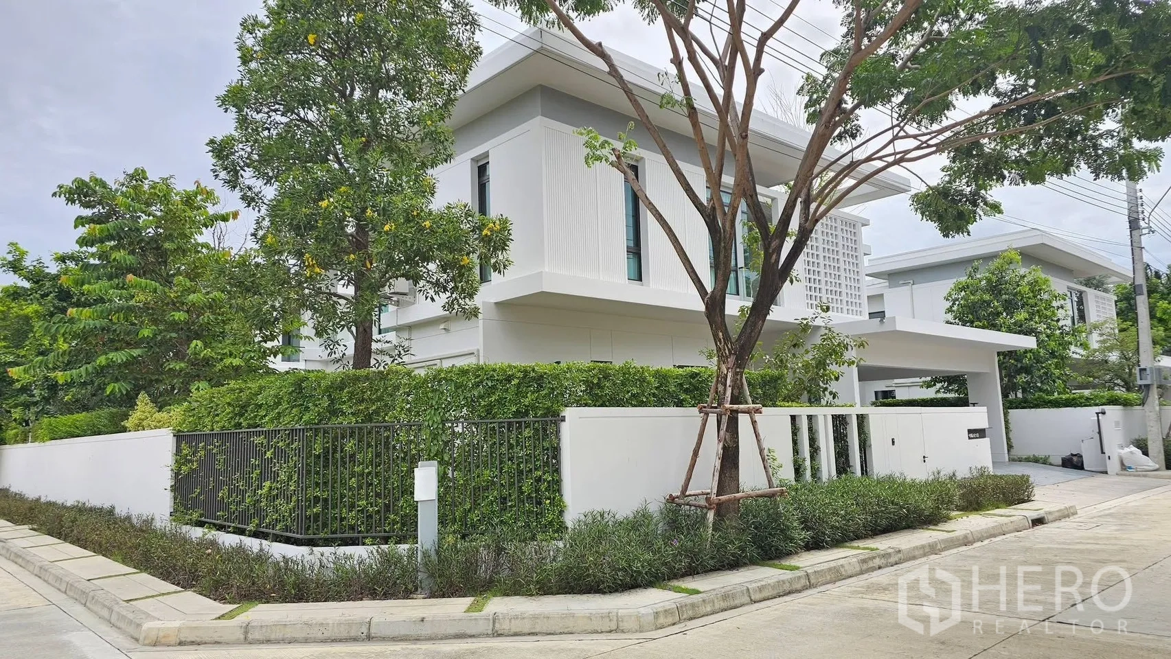 独栋房屋 for rent in Bang Phli, Samut Prakan - 现代白色两层独栋别墅，绿化与围篱环绕。