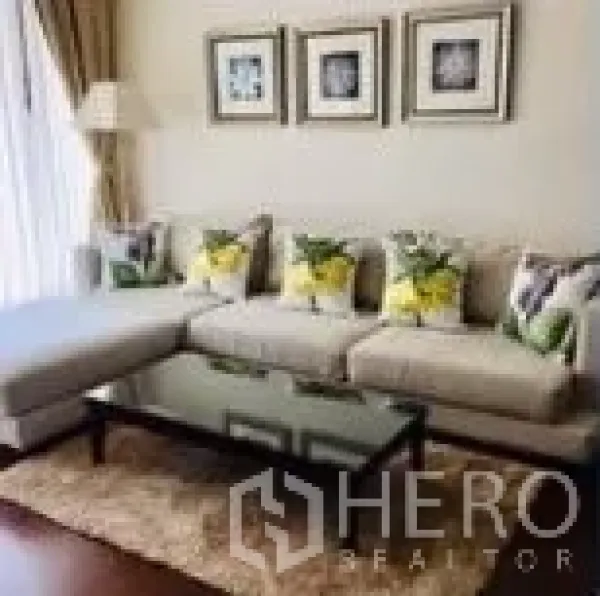 Condominium for rent in Watthana, Bangkok - Cozy lounge with L-shaped sofa, glass coffee table, rug and framed wall art.