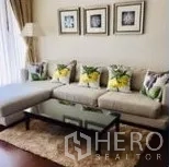 Condominium for rent in Watthana, Bangkok - Cozy lounge with L-shaped sofa, glass coffee table, rug and framed wall art.