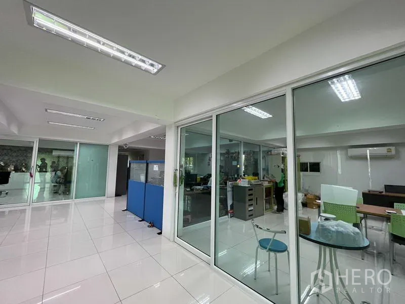 Warehouse for rent or sale in Nonthaburi - Open-plan office area with glass partitions, tiled floor, and fluorescent lighting.