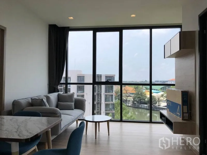 公寓 出租在Watthana, Bangkok - 采光明亮的客厅，落地窗、沙发与用餐区，可眺望运河与城市景观。