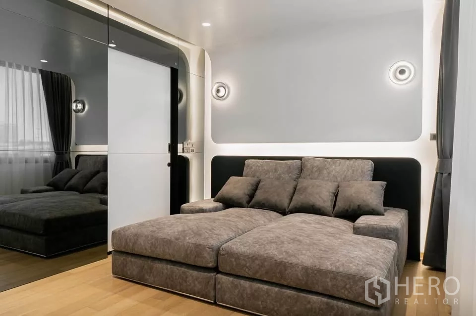 Townhouse for sale in Chatuchak, Bangkok - Media room with grey chaise sofa and mirrored sliding wardrobe.