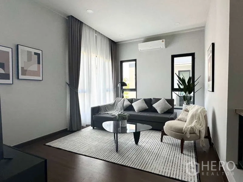 บ้าน ให้เช่าในBang Phli, Samut Prakan - ห้องนั่งเล่นสบาย โซฟาสีเทา โต๊ะกาแฟทรงกลม และหน้าต่างบานใหญ่