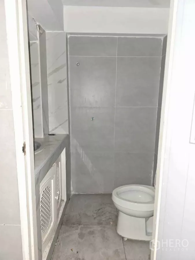 Retail Space for rent in Watthana, Bangkok - Compact bathroom with gray wall tiles, toilet and built-in sink counter inside the shop.