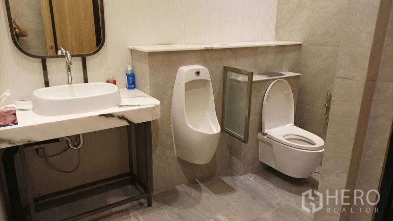 Retail Space for rent - Restroom with marble vanity, urinal and toilet with bidet spray in gray tiles.