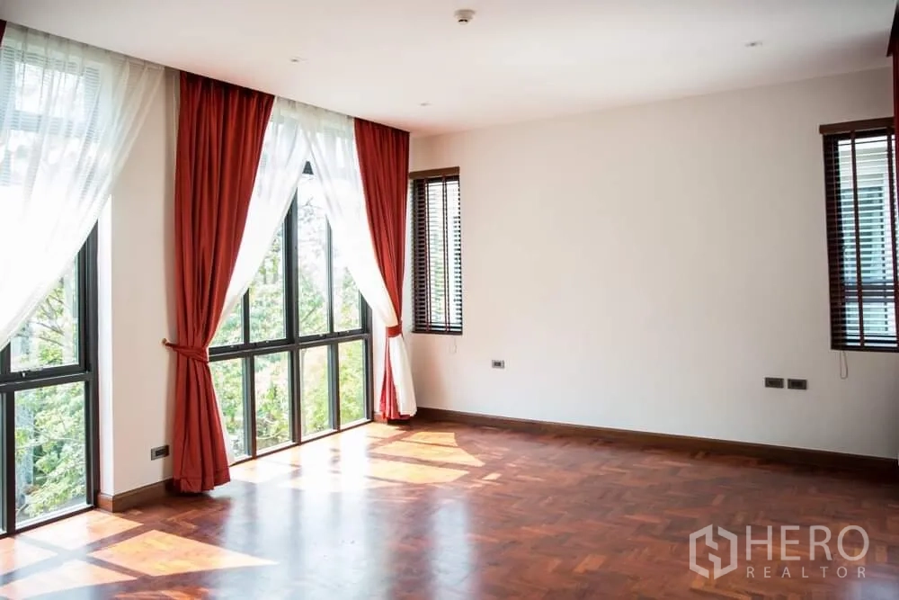 Detached House for rent in Khlong Toei, Bangkok - Large corner bedroom with parquet wood floor and full-height windows with red drapes.