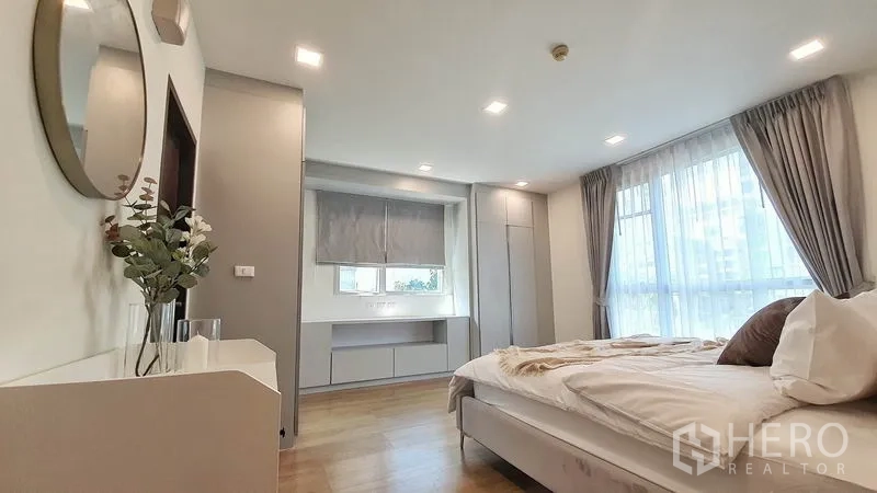 Condominium for rent in Khlong Toei, Bangkok - Master bedroom facing large curtained windows with built-in storage and a desk along one wall.