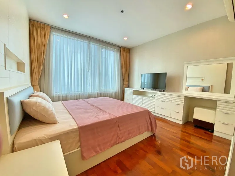 Condominium for rent in Khlong Toei, Bangkok - Master bedroom with large window, pink bedding, TV cabinet and dressing vanity.