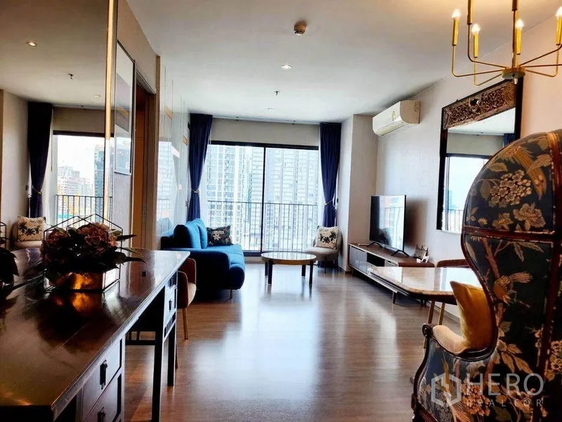 公寓 出租在Watthana, Bangkok - 明亮客厅，木地板、蓝色沙发、电视柜，落地窗通向阳台，俯瞰曼谷天际线。