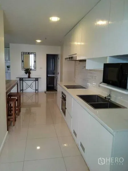 Condominium for rent in Khlong Toei, Bangkok - Bright galley kitchen with white cabinets, built-in hob, sink and microwave.