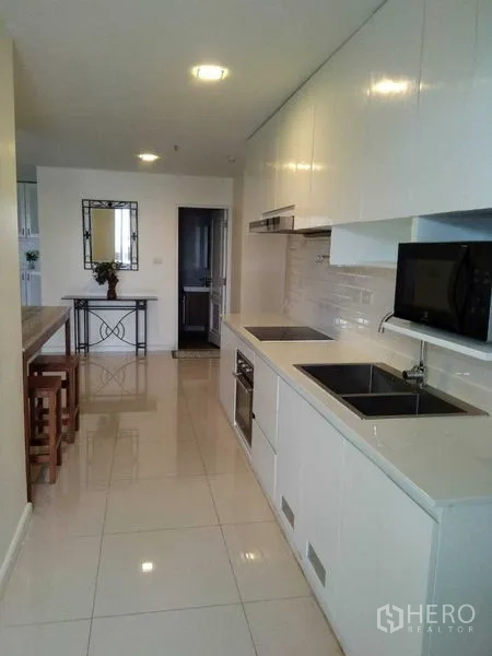 Condominium for rent in Khlong Toei, Bangkok - Bright galley kitchen with white cabinets, built-in hob, sink and microwave.