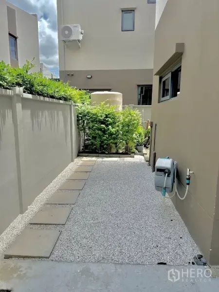 独立式住宅 出租或出售在Prawet, Bangkok - 侧院铺石小径与碎石地面，墙边设有水管卷盘。