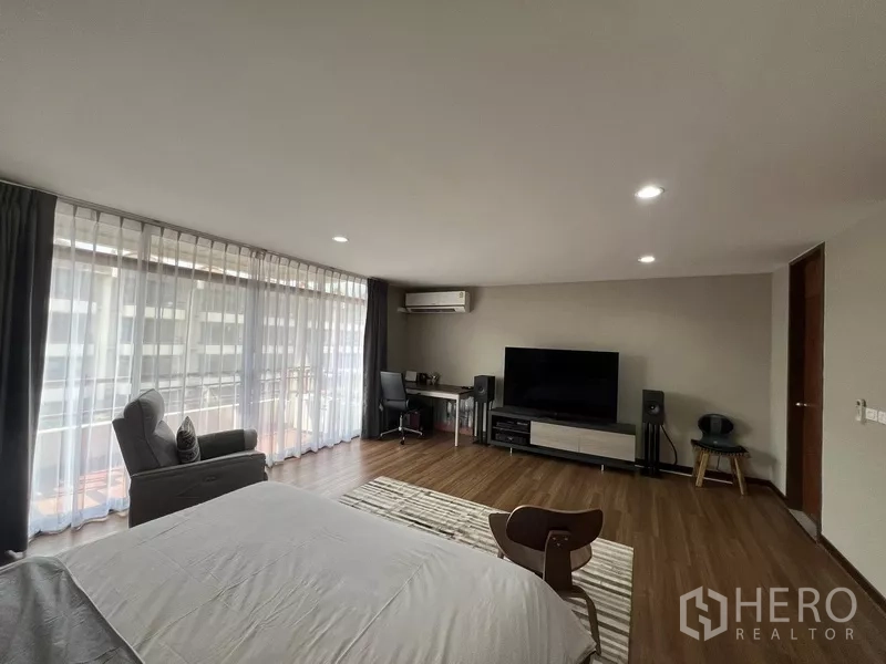Townhouse for rent or sale in Suan Luang, Bangkok - Large bedroom with TV, desk, wide windows and balcony access.