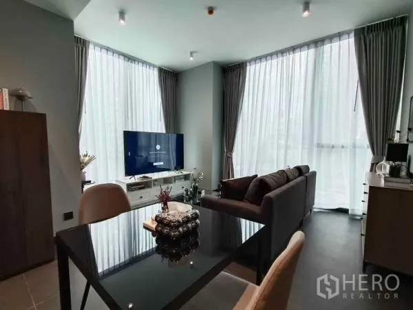 公寓 出租在Bang Rak, Bangkok - 开放式客厅与餐区，落地窗、灰色沙发、电视与玻璃餐桌，Tait Sathorn 12。