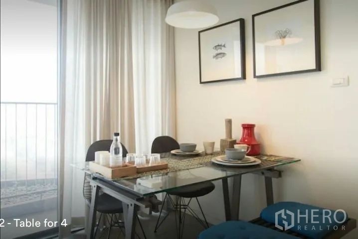 Condominium for rent in Phaya Thai, Bangkok - Dining nook with a glass table set for four beside a balcony window and sheer curtains.