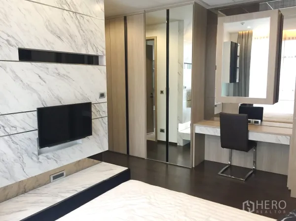Condominium for rent in Watthana, Bangkok - Bedroom with marble feature wall, wall-mounted TV, mirrored wardrobe and dressing table.