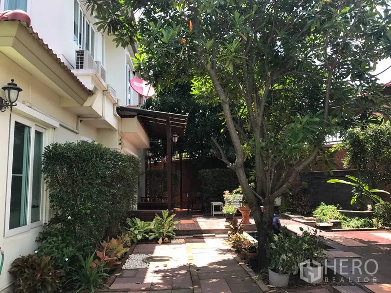 独立式住宅 出售在Pak Kret, Nonthaburi - 房侧铺砖庭院，成树、雨棚与步道。