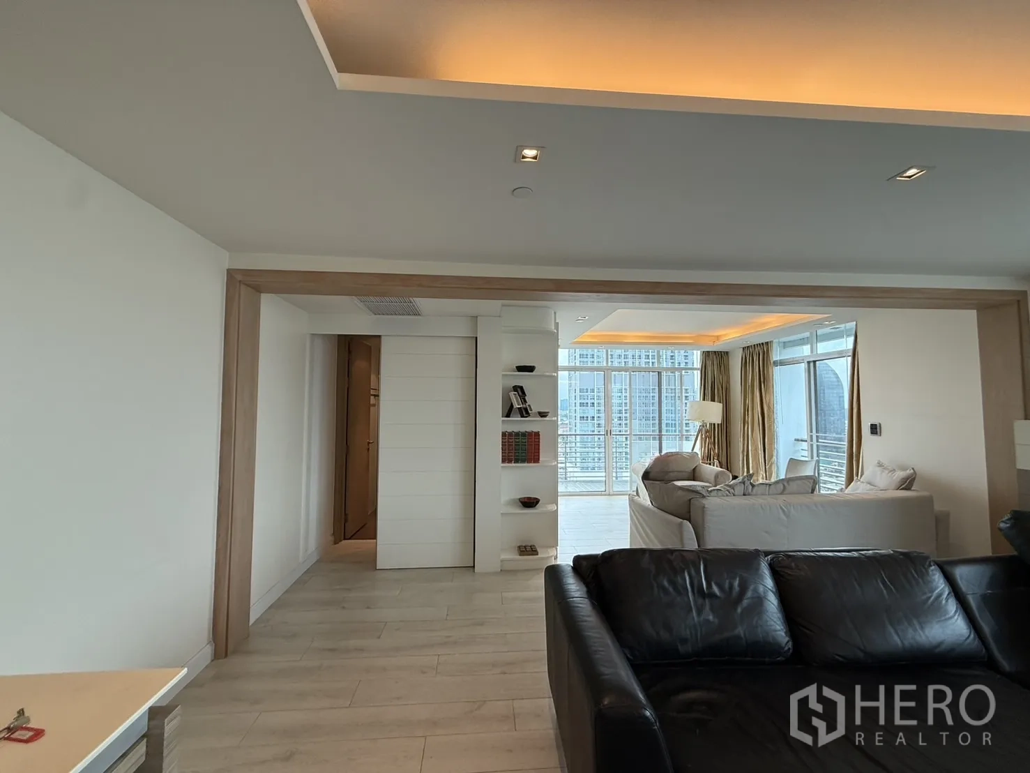 Condominium for rent in Phaya Thai, Bangkok - Open layout from leather sofa toward a cozy sitting room with built‑in shelving and city views.