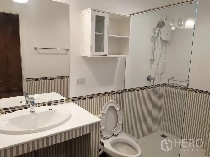Townhouse for rent in Mueang Samut Prakan, Samut Prakan - Bathroom with glass-enclosed shower, vanity basin, and striped wall tiles.