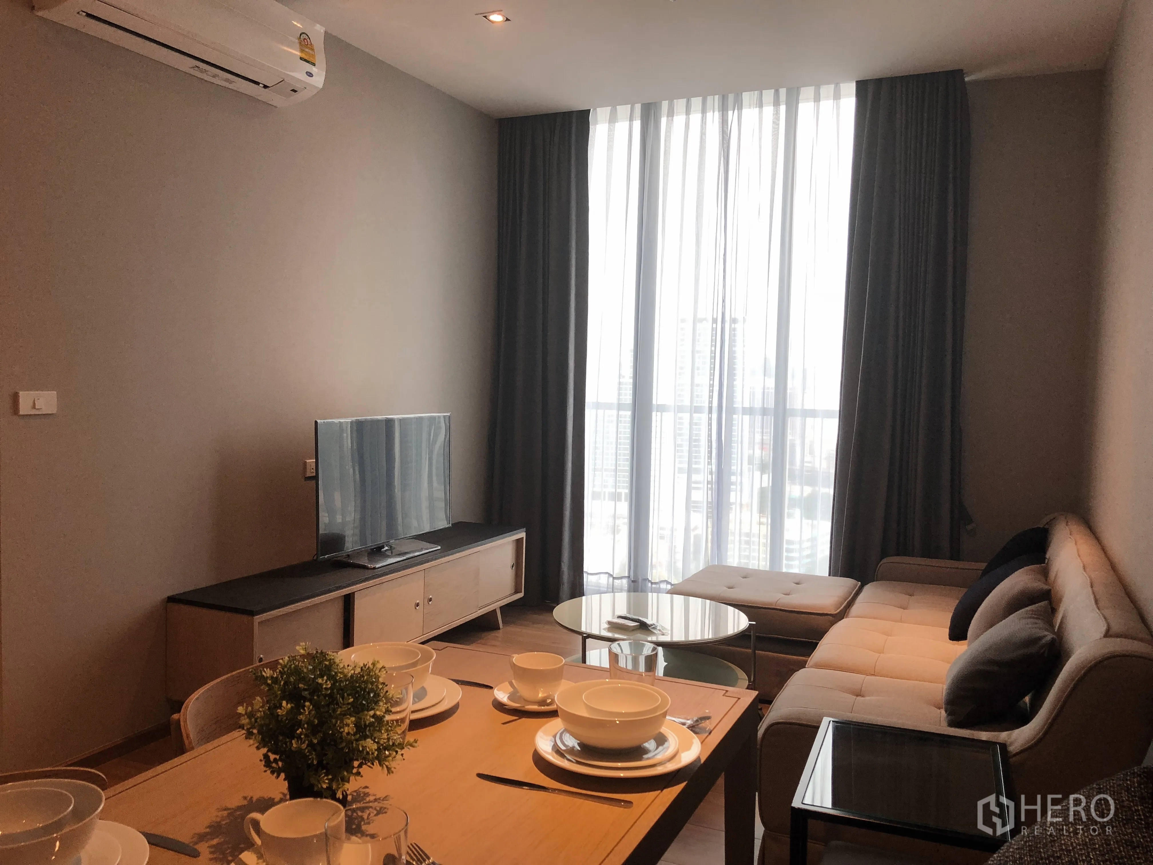 Condominium for rent in Khlong Toei, Bangkok - Bright living and dining area with floor-to-ceiling windows, sofa and TV overlooking the city.