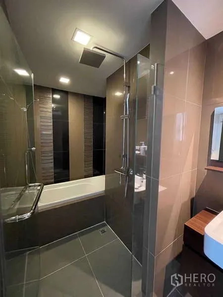 Condominium for sale in Watthana, Bangkok - Modern bathroom with glass shower enclosure, rain shower and separate bathtub.