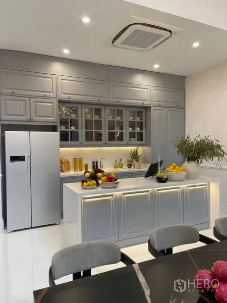 Detached House for sale in Suan Luang, Bangkok - Contemporary kitchen with island, grey cabinetry and double-door refrigerator beside a dining space.