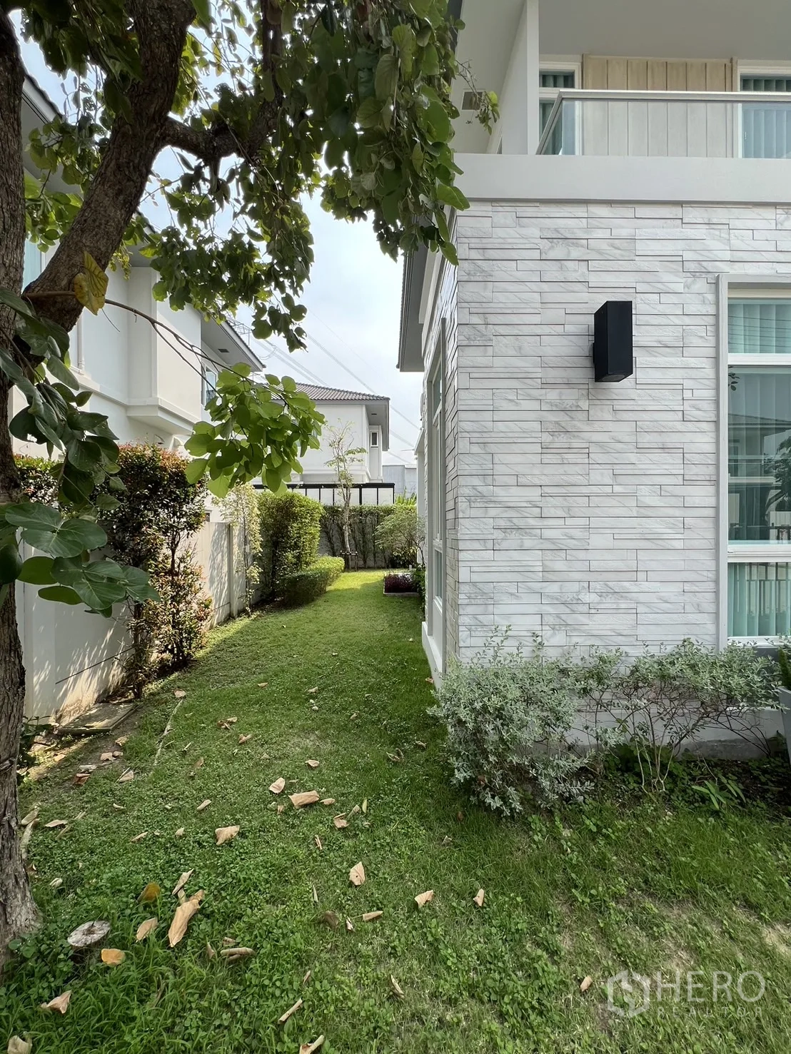 独立式住宅 出租在Prawet, Bangkok - 树荫侧院与石材纹理外墙及灌木。