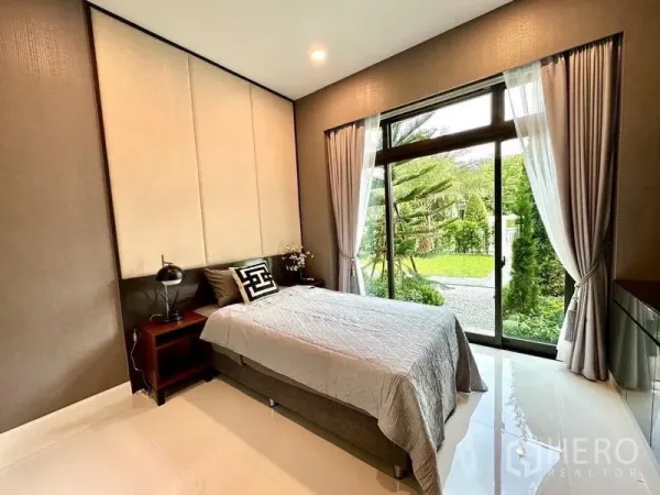 独立式住宅 出租在Lat Krabang, Bangkok - 一层卧室，落地窗面向花园，浅色窗帘与中性色调