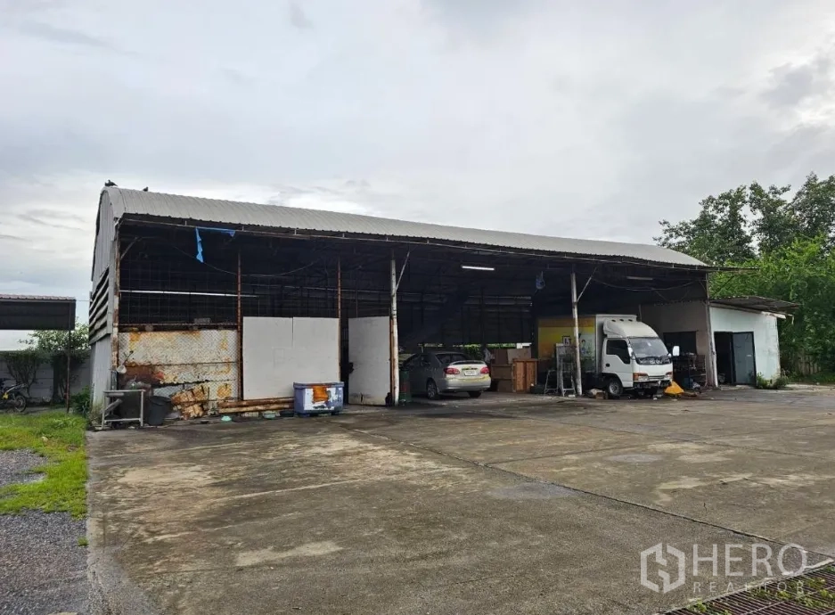 Warehouse for rent in Lam Luk Ka, Pathum Thani - Detached workshop shed with open bays and vehicles inside.